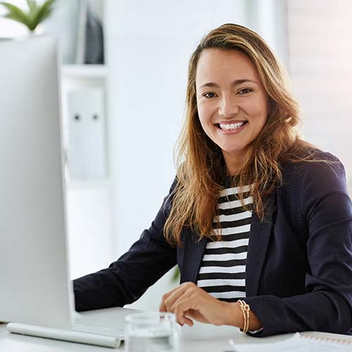Mujer sonríe en su oficina, frente al computador lee sobre cesantías para empresas en Protección