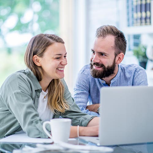 Pareja de esposos en su casa, disfruta de un café mientras lee en el portátil sobre Certifácil de Protección