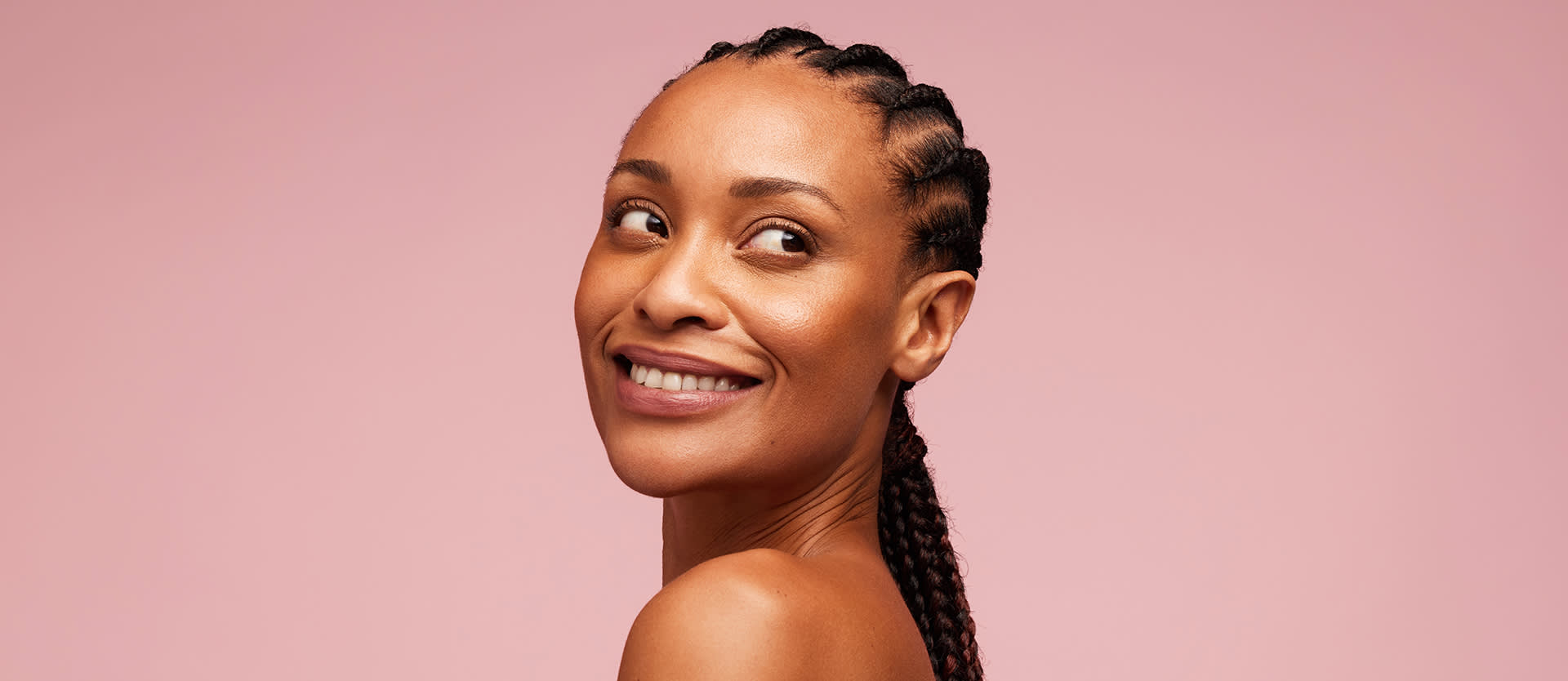 Black woman with clean and clear skin looking away. Female model having braided hairstyle standing against pink background.