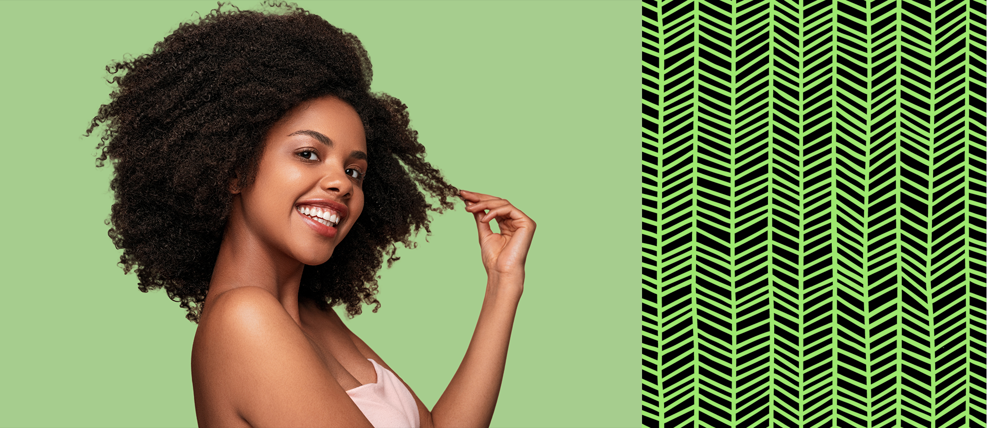 Side view of positive African American female model smiling for camera and touching clean curly hair after hygienic routine against brown background