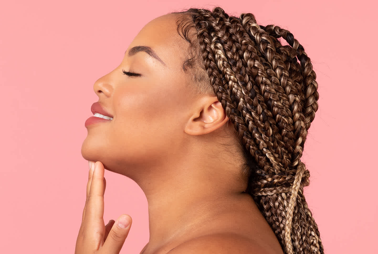 Profile portrait of beautiful black woman with perfect skin touching her chin over pink studio background with braided hair