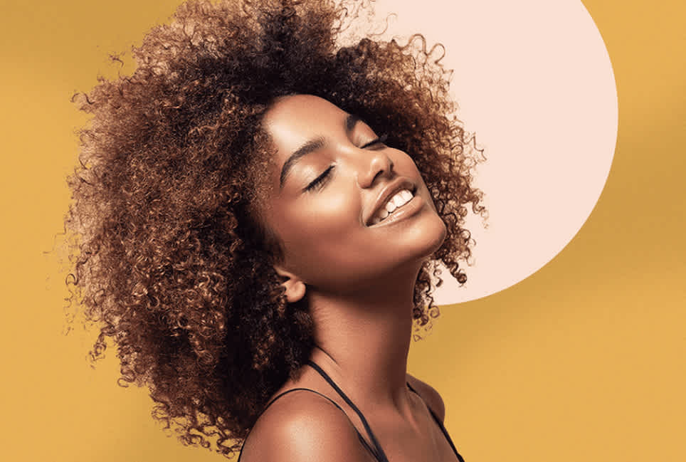 Woman with natural curls gazing up with eyes closed against a gold background