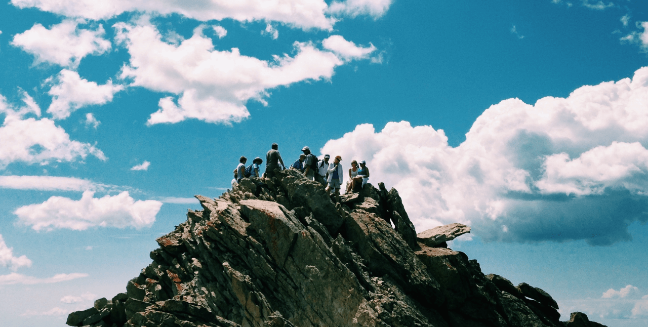 Image of a team at the top of a mountain, with blue sky and white clouds