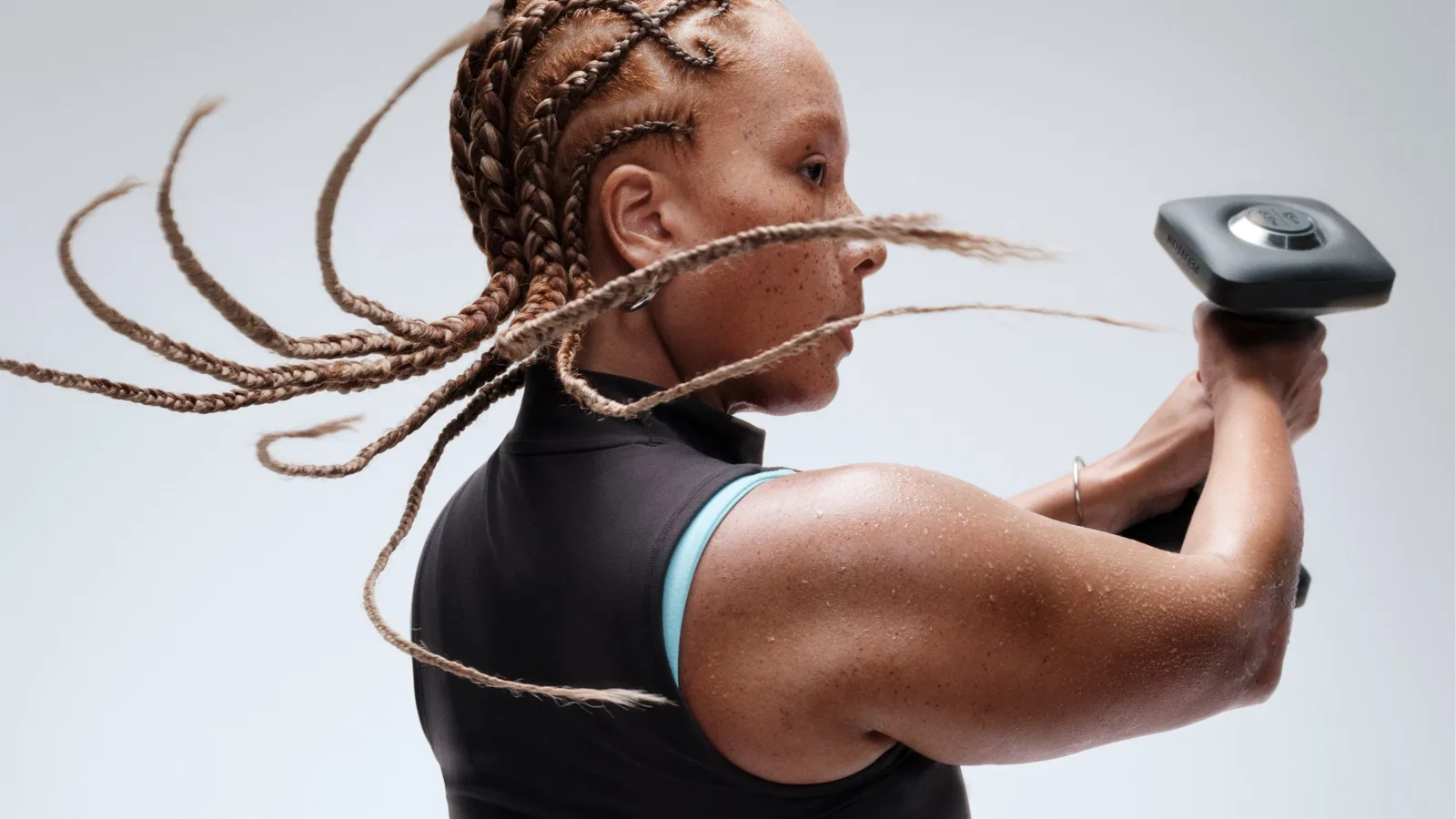 A close-up of a woman swinging a dumbbell with her hair whipping around.