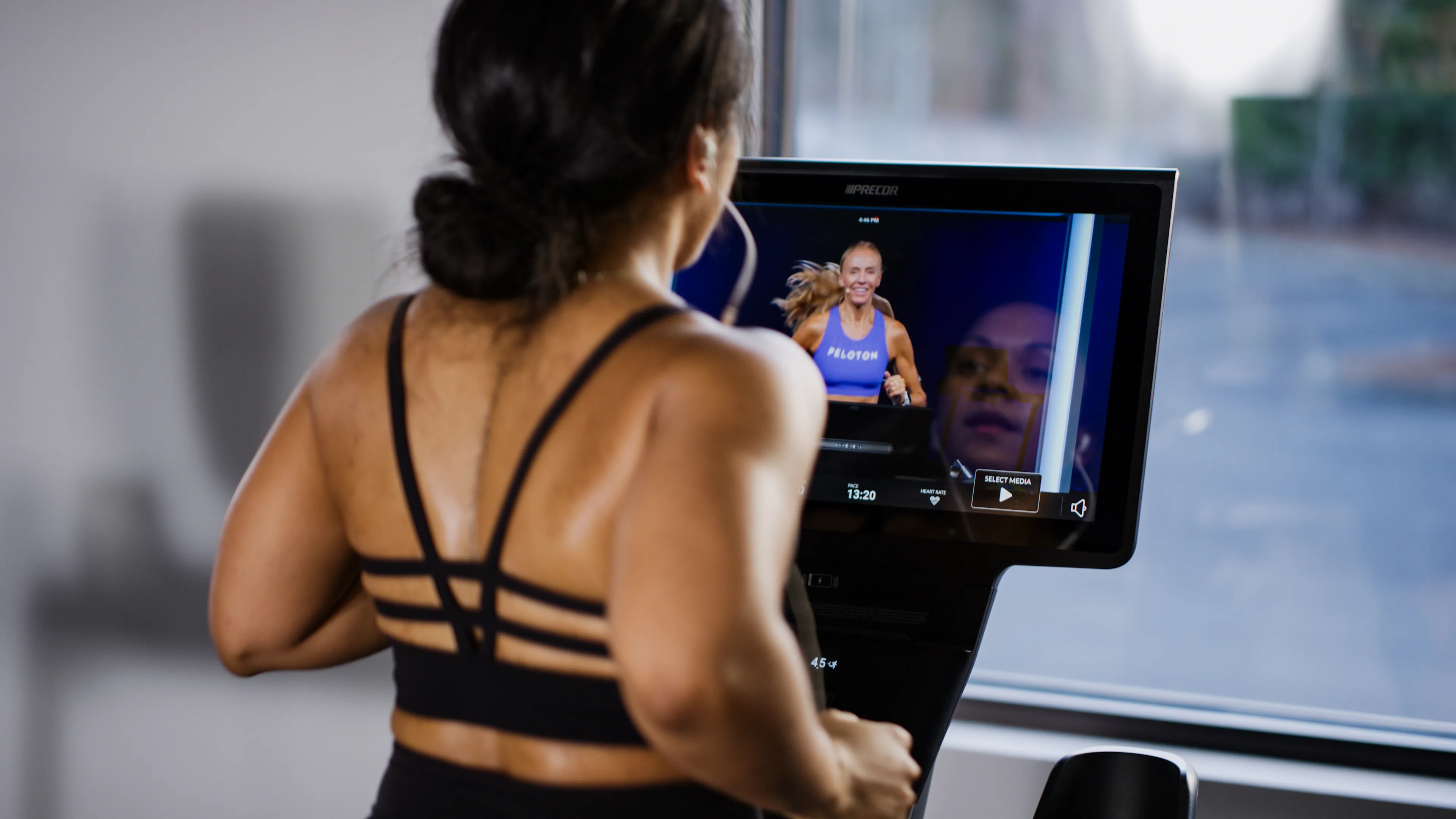 An exerciser using a Precor treadmill showing Peloton workouts