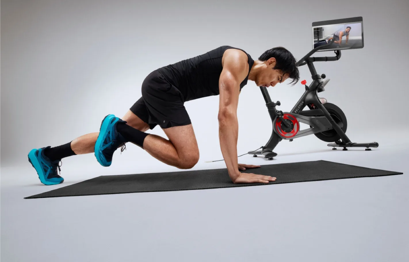 A person exercising on the mat next to their Peloton Bike+ Pro.