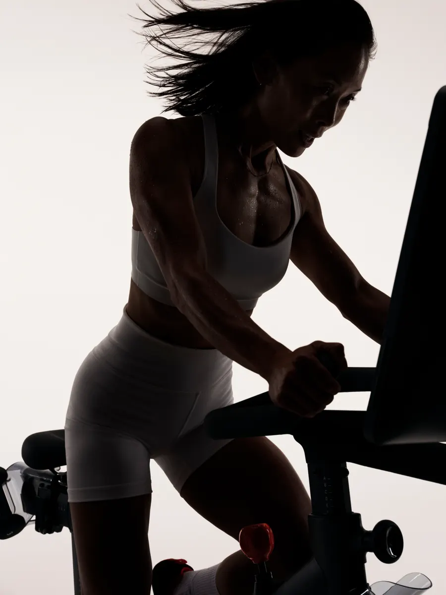 A woman standing while riding  Peloton Bike Pro with a dark shadow cast over her.