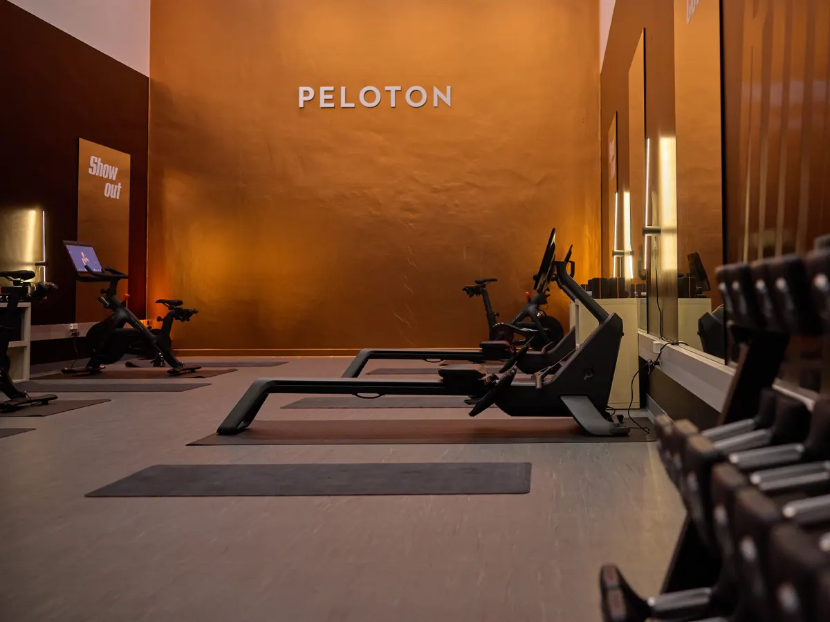 An interior view of a Peloton Spaces environment with copper colored walls, a Peloton logo on the wall, and Peloton equipment ready for use.