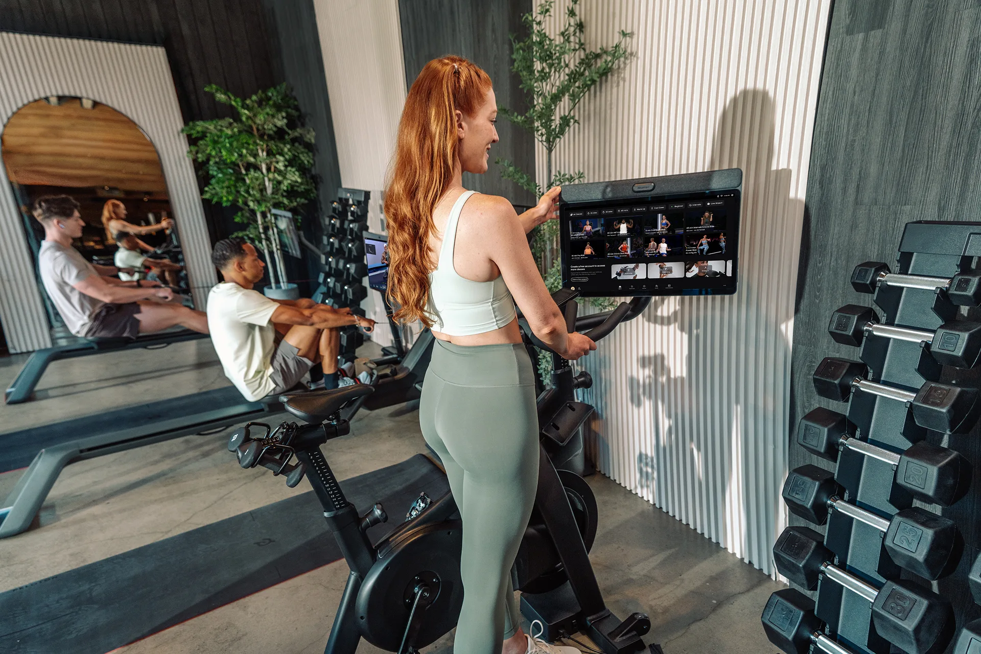 Person standing beside a commercial exercise bike, tapping the touchscreen display