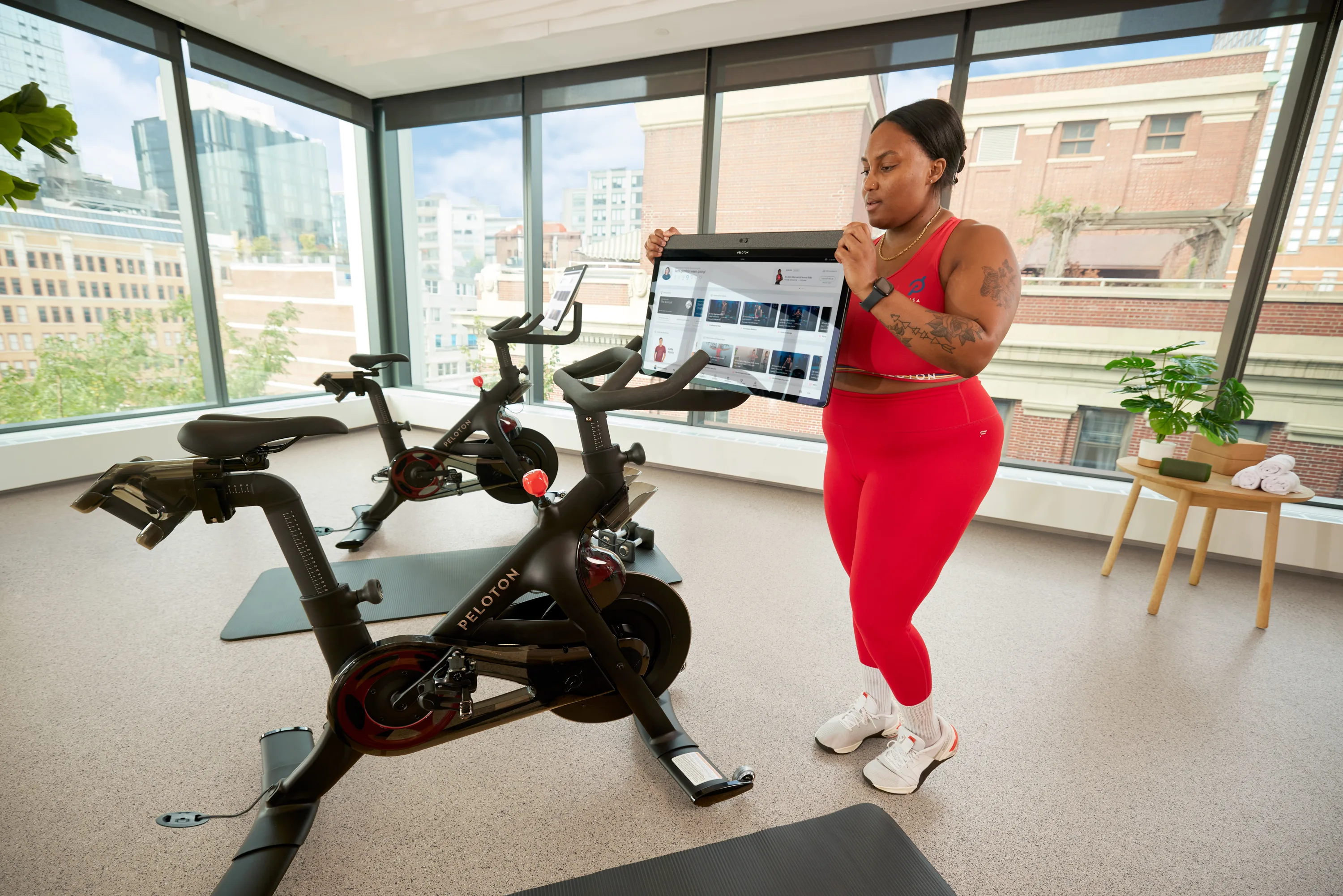 An exerciser standing in front of a Peloton Bike+, turning the screen towards a mat next to the Bike+ to do an off-the-Bike workout