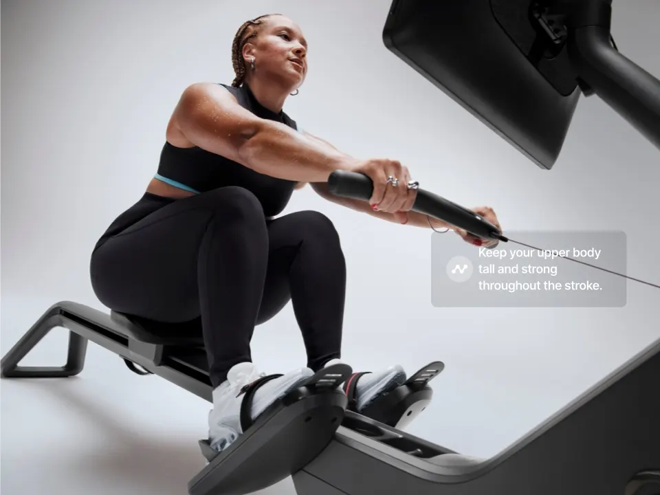 A woman on the Peloton Row+ Pro with an overlay on top that says, "Keep your upper body tall and strong throughout the stroke"