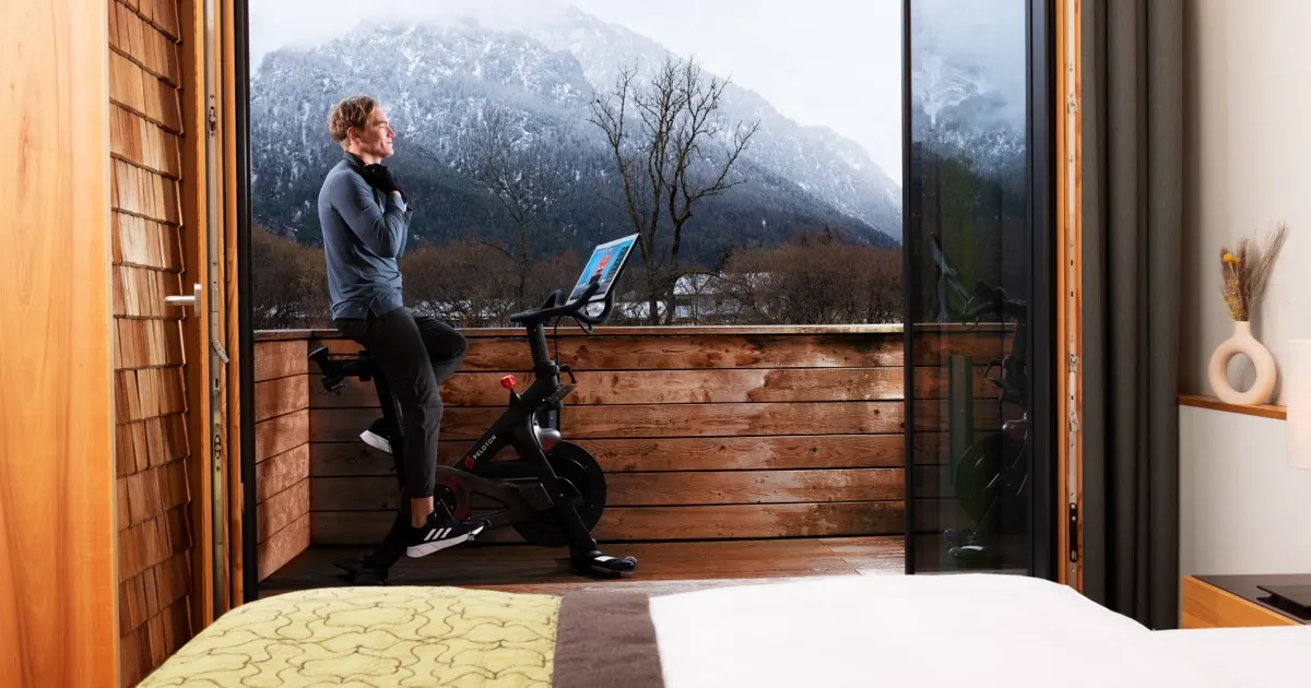 Gast trainiert am Morgen auf dem Peloton Bike auf dem Balkon seiner Suite, während die Alpen im Hintergrund zu sehen sind. 