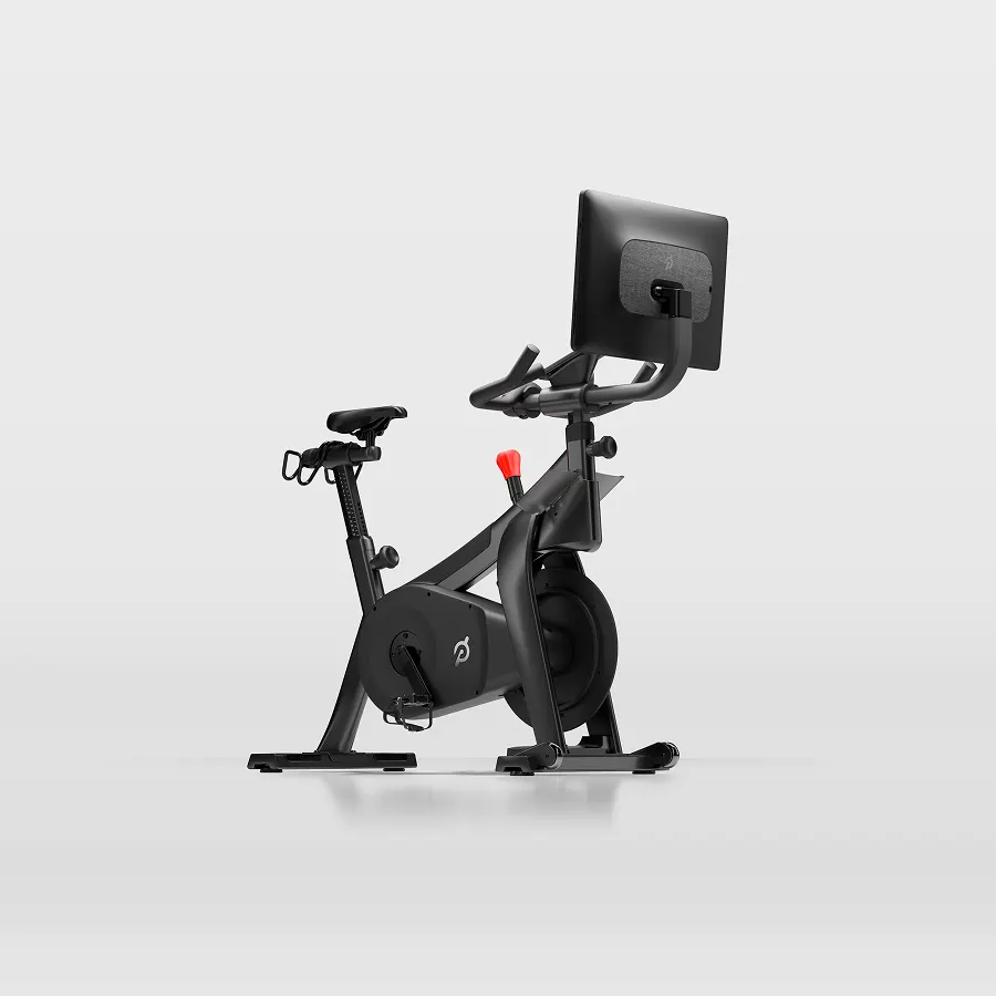 Side profile of the Peloton Commercial Bike, featuring its dark frame, adjustable seat, handlebars, and large front touchscreen