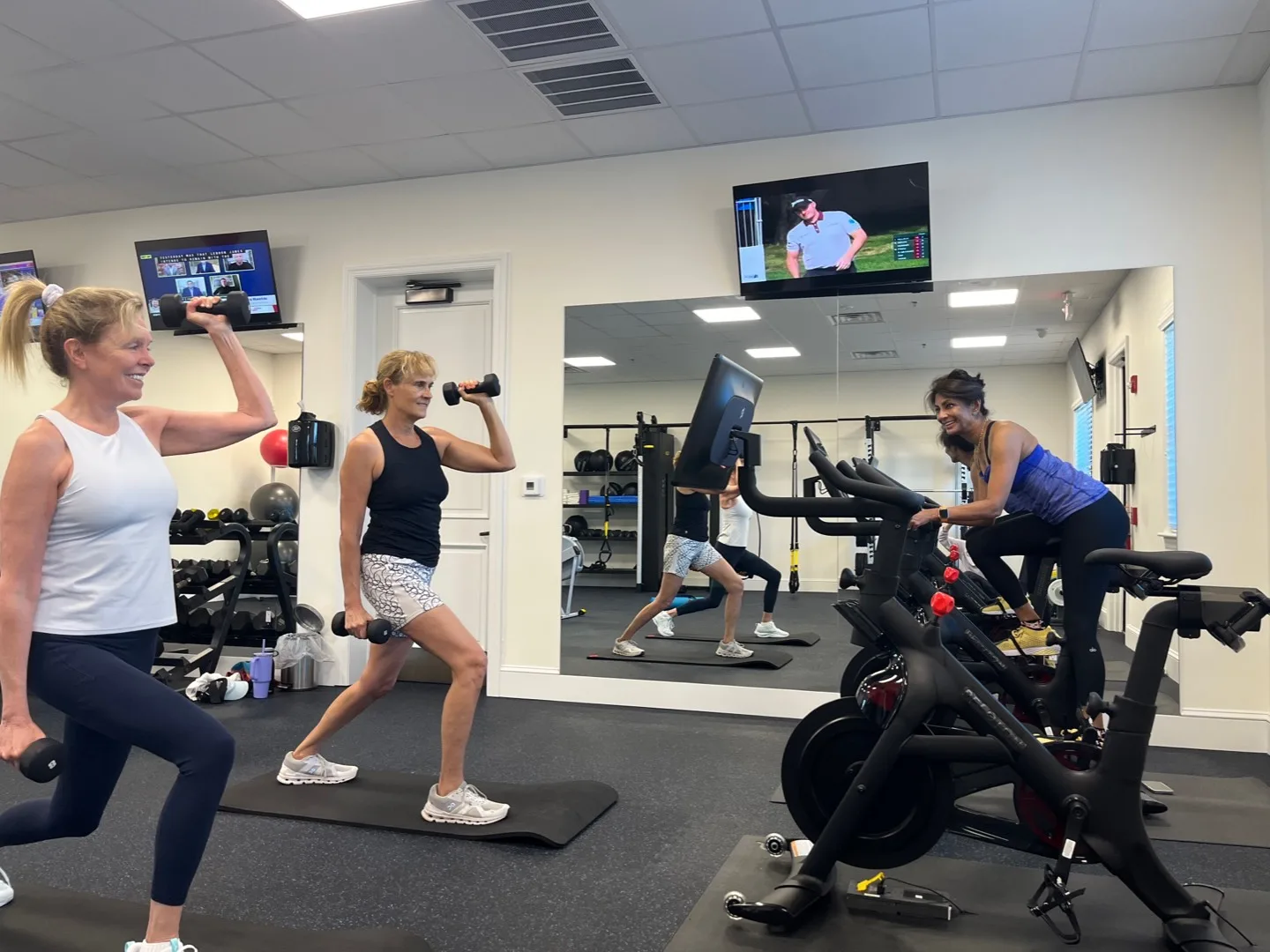 3 exercisers working out in a gym, one of them using a Peloton Bike