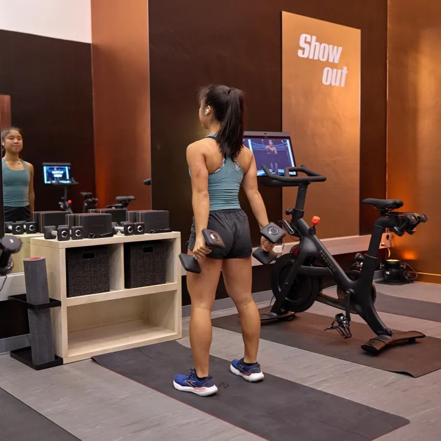 An exerciser using a cross-functional Peloton Bike for a strength class