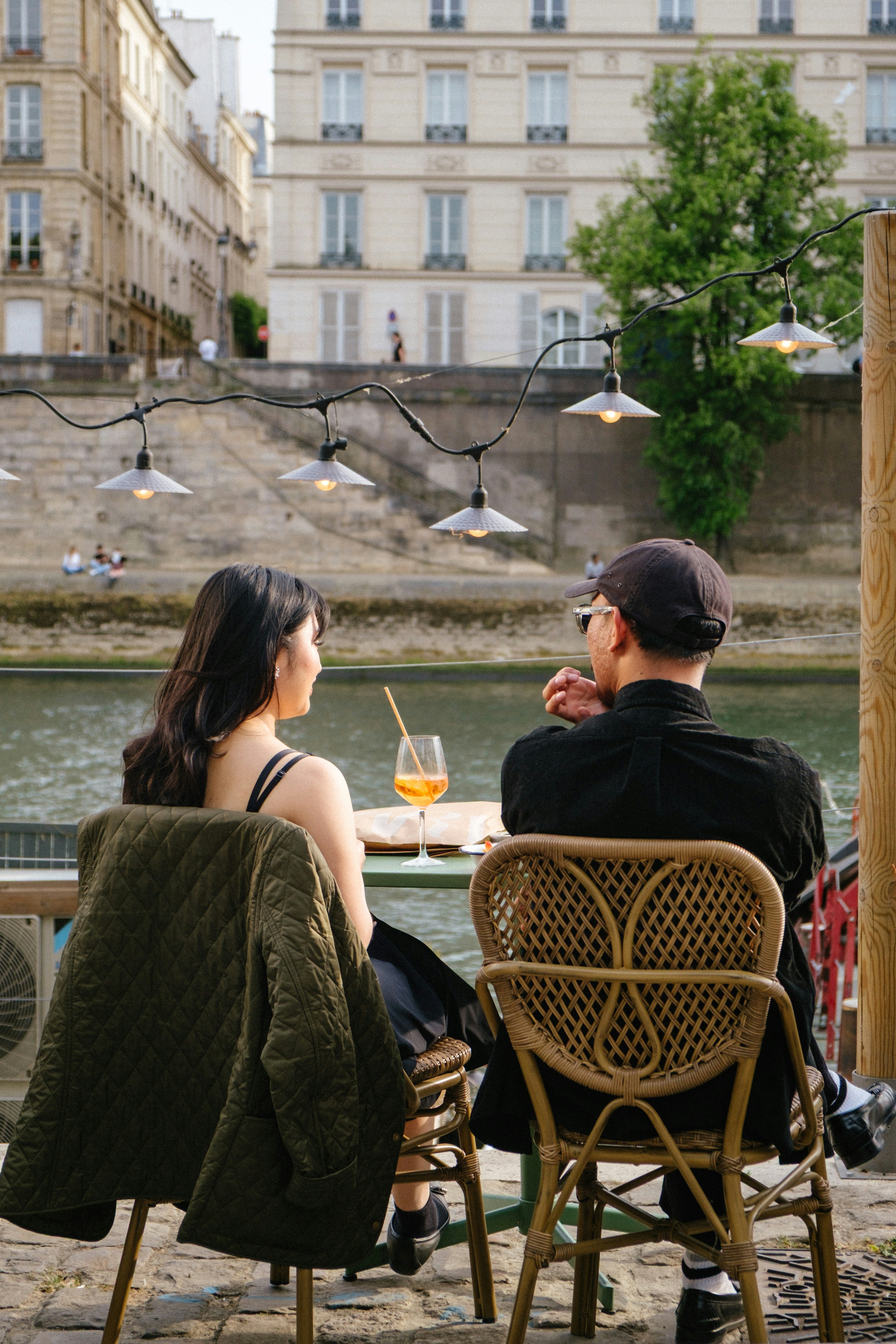 couple, girl, woman and man on cafe chairs by water in city