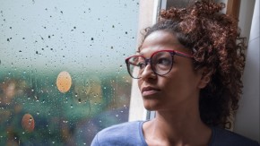 Depressed woman looking out at rain through window