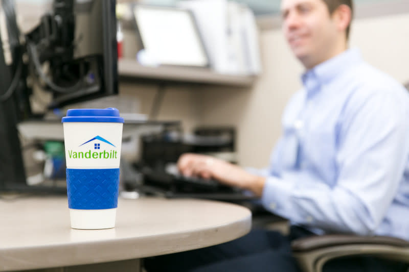 A man sits at a desk working on his computer with his Vanderbilt Mortgage and Finance, Inc. cup beside him.