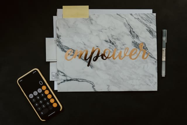 A flat lay of a folder that reads "empower" on the front with a calculator on one side of it and a pen on the other.