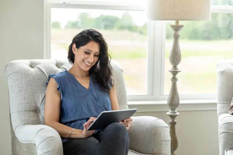 A woman sitting on chair looking at tablet.