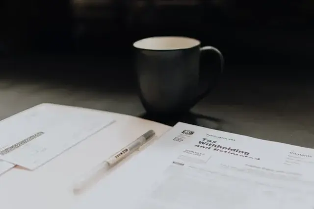 A manila folder is open on a desk with tax documents and a clear pen inside with a black coffee mug above. 