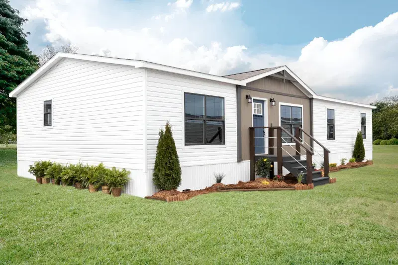 Exterior of a white manufactured home with a small front porch under a blue sky.