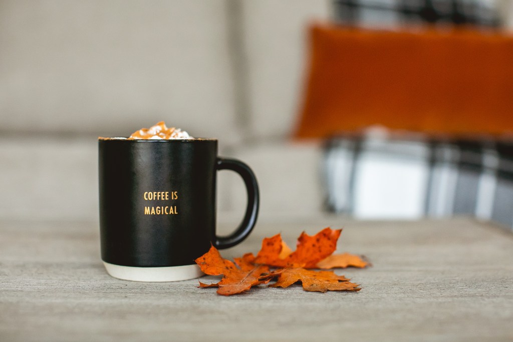Cup of coffee with whip cream and caramel on a table next to fall leaves.