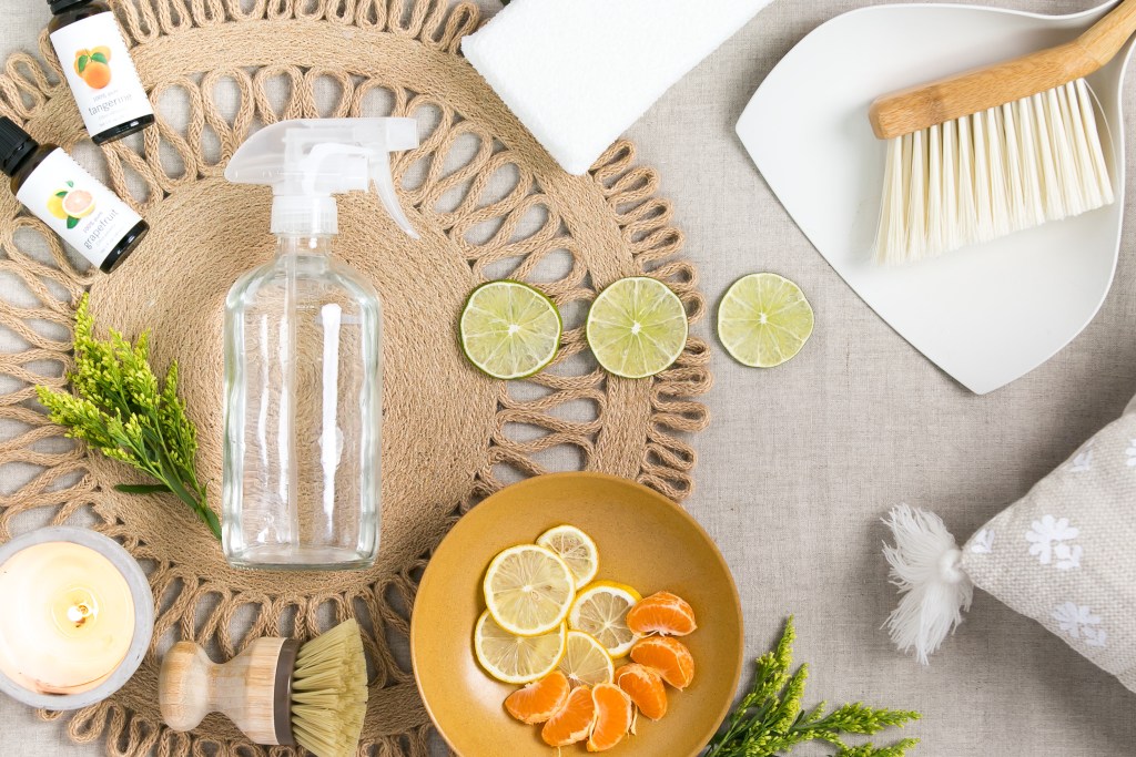 Cleaning supplies, spray bottle, limes, oranges, scrubber, and handheld broom. 