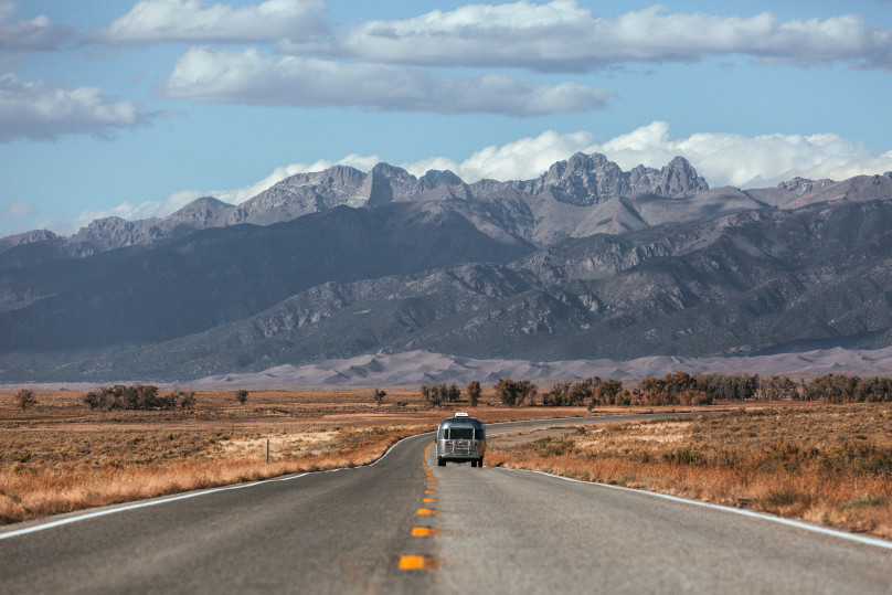 A camper riding down a road with mountains in distance.