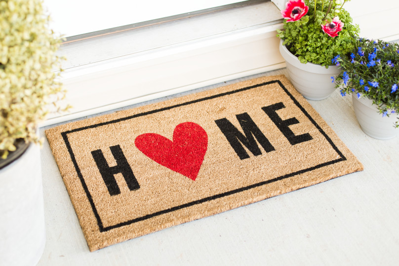 A welcome mat that reads HOME with potted plants beside it.