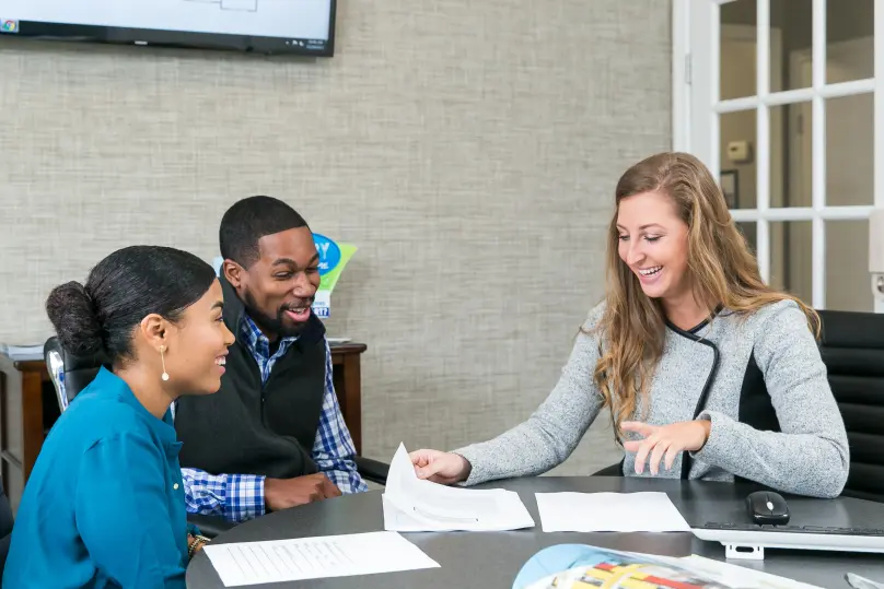 A young couple smiling and looking at paperwork at a table with a smiling young woman