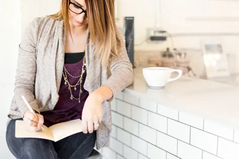 Young woman is sitting at a coffee bar with a notebook taking notes. 