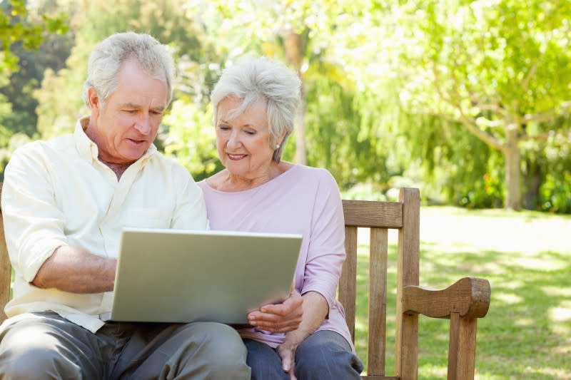An elderly couple looking at computer together on bench.