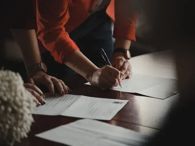 Two women at table, one signing a document.