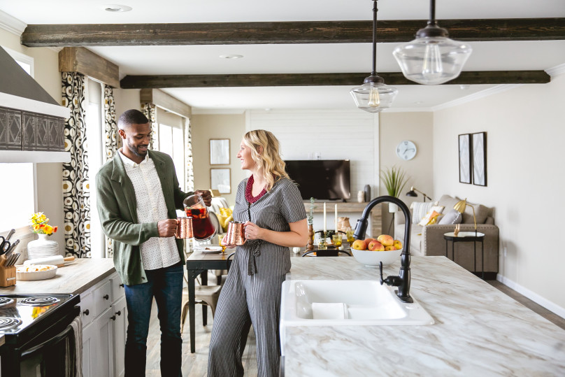 A man and woman stand in the kitchen of a new manufactured home, drinking and smiling.