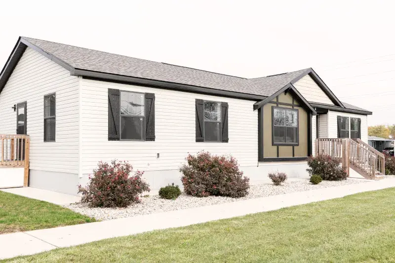 The exterior of a manufactured home with white siding and black trim and shutters.