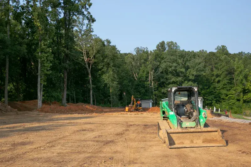 A site being prepared by leveling the land with construction vehicles working on the land surrounded by green woods. 