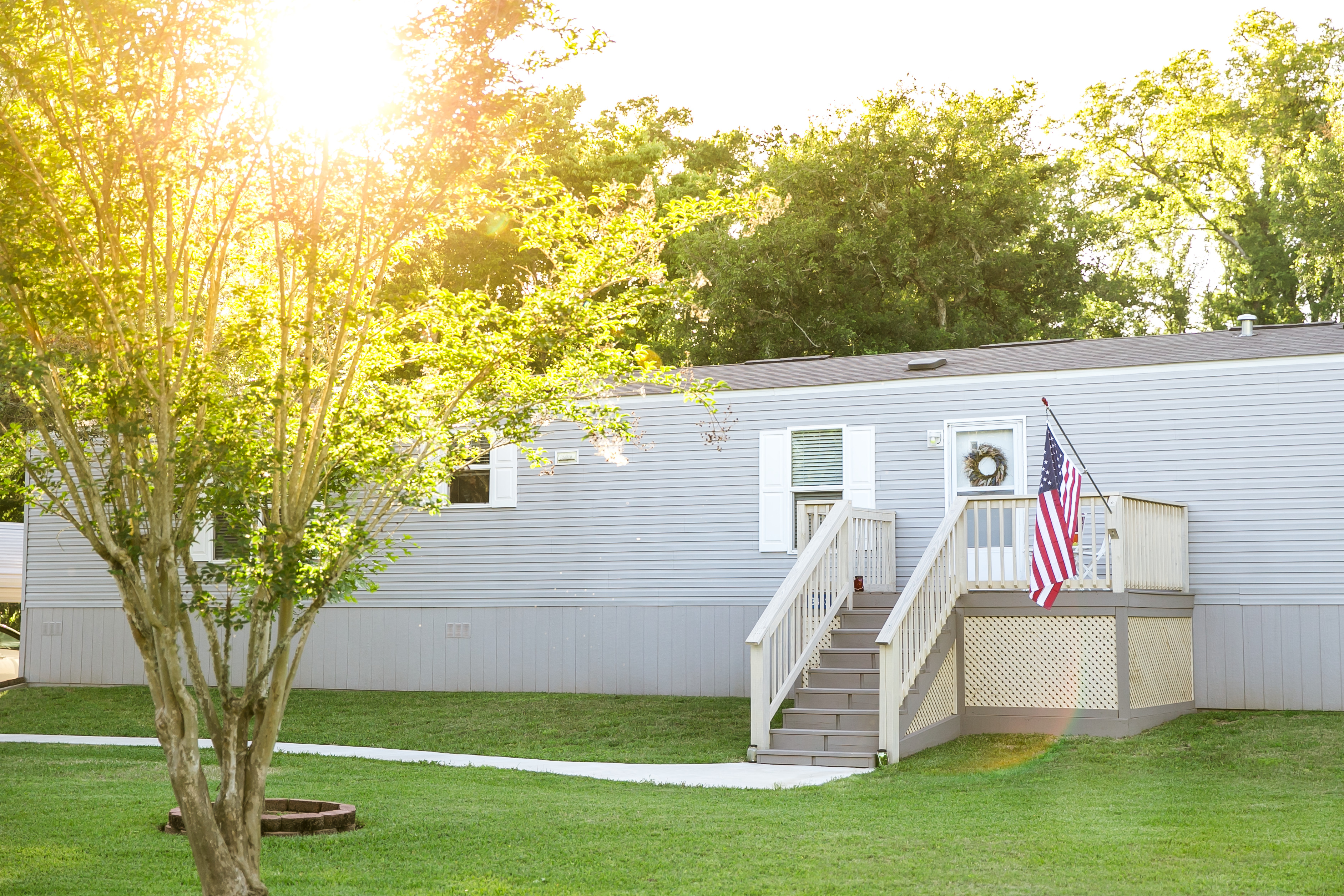 gray mobile home with tree and flag in front 