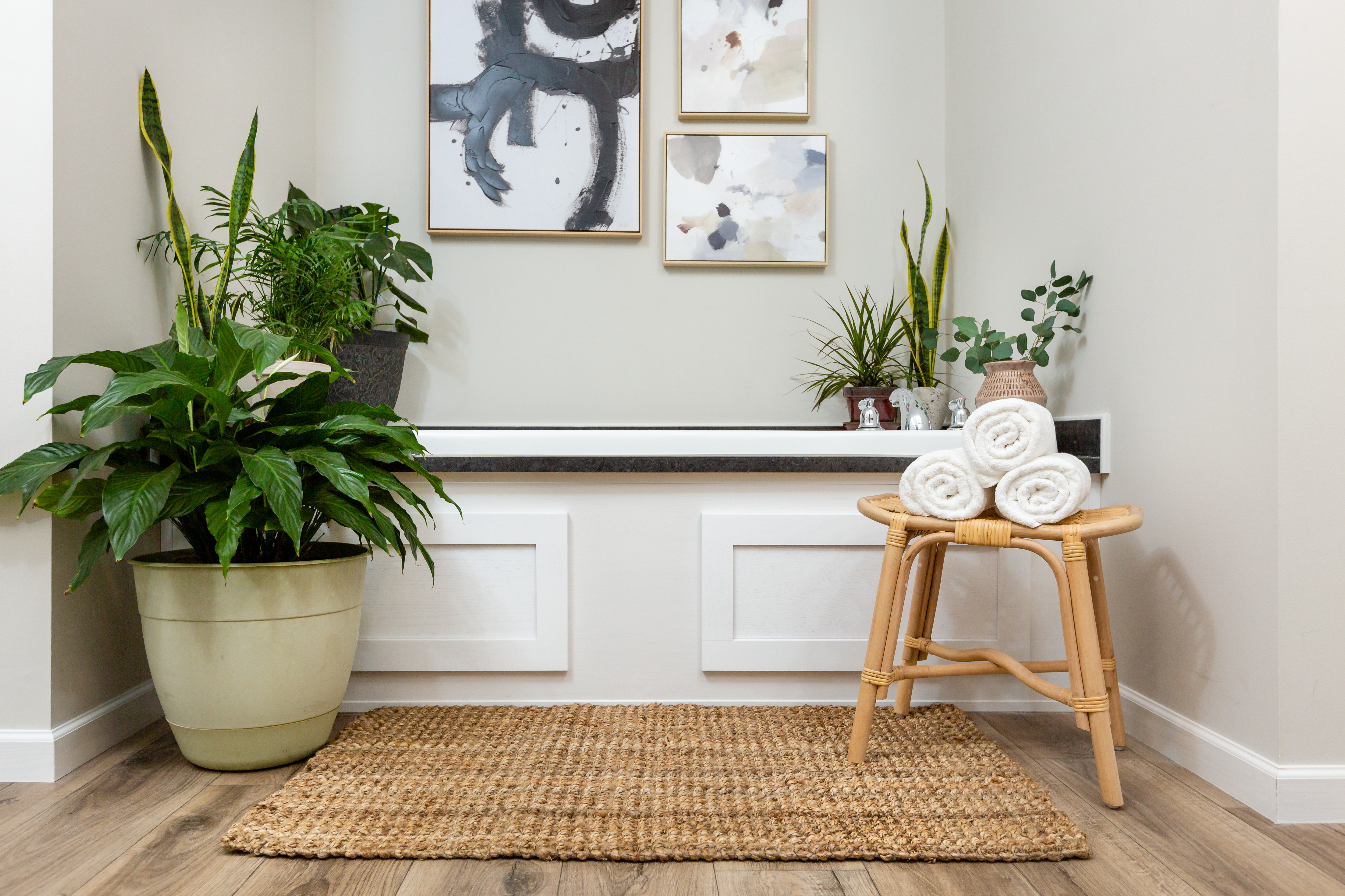 Bathtub with potted plant and stool with towels in front of it 