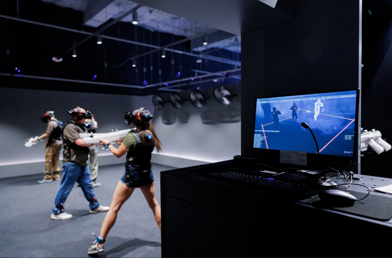 A split screen of a group playing immersive full body VR, with a computer screen showing what they are seeing in their VR headsets. 