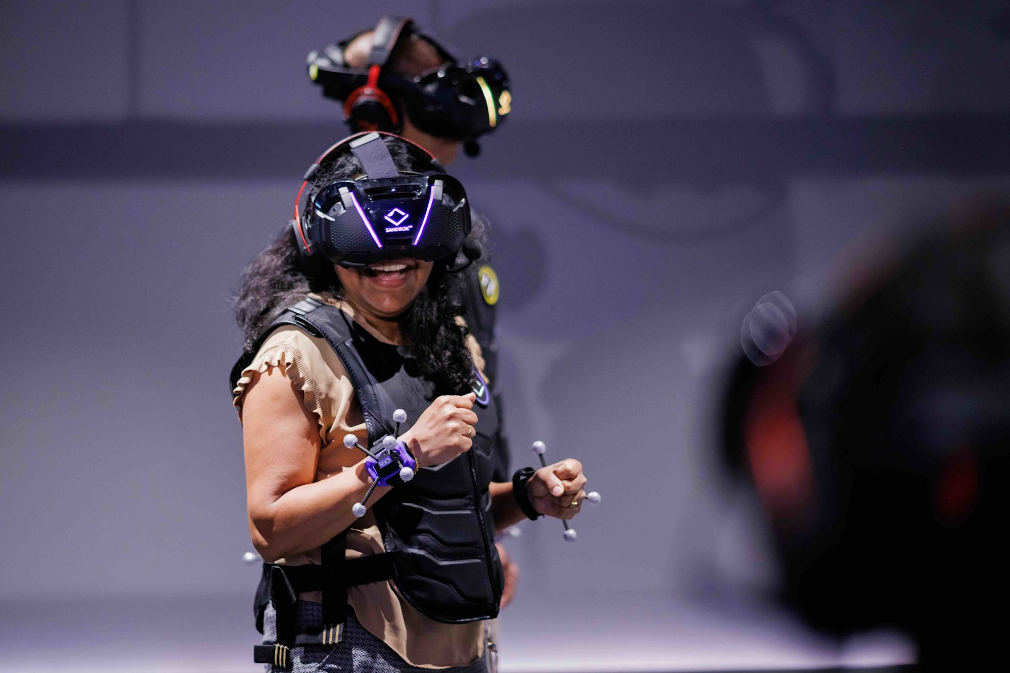 Lachende Spielerin mit VR-Headset und Weste in der Spielfläche