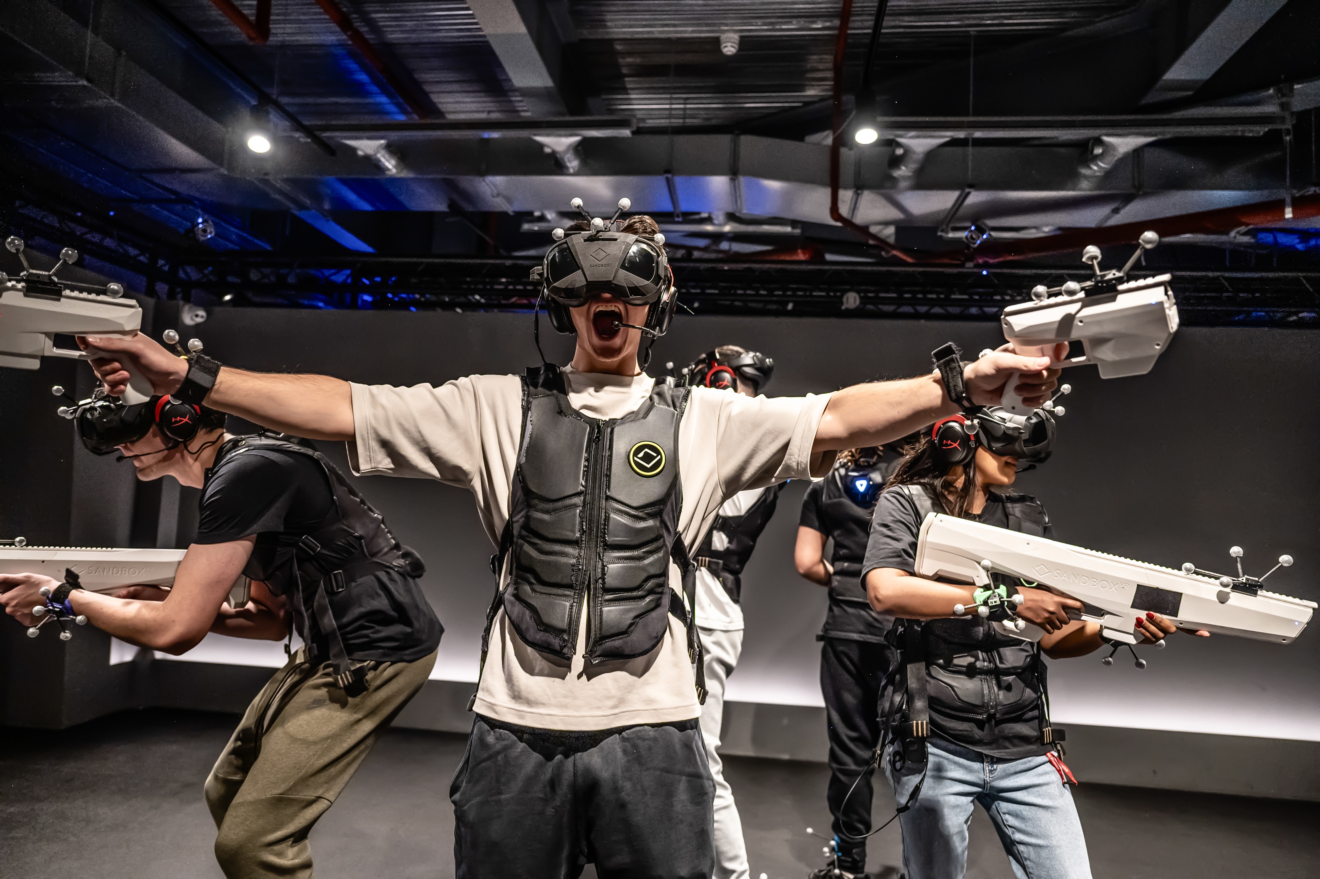 A group of players wearing VR headsets and haptic vests battle together in an immersive VR experience.