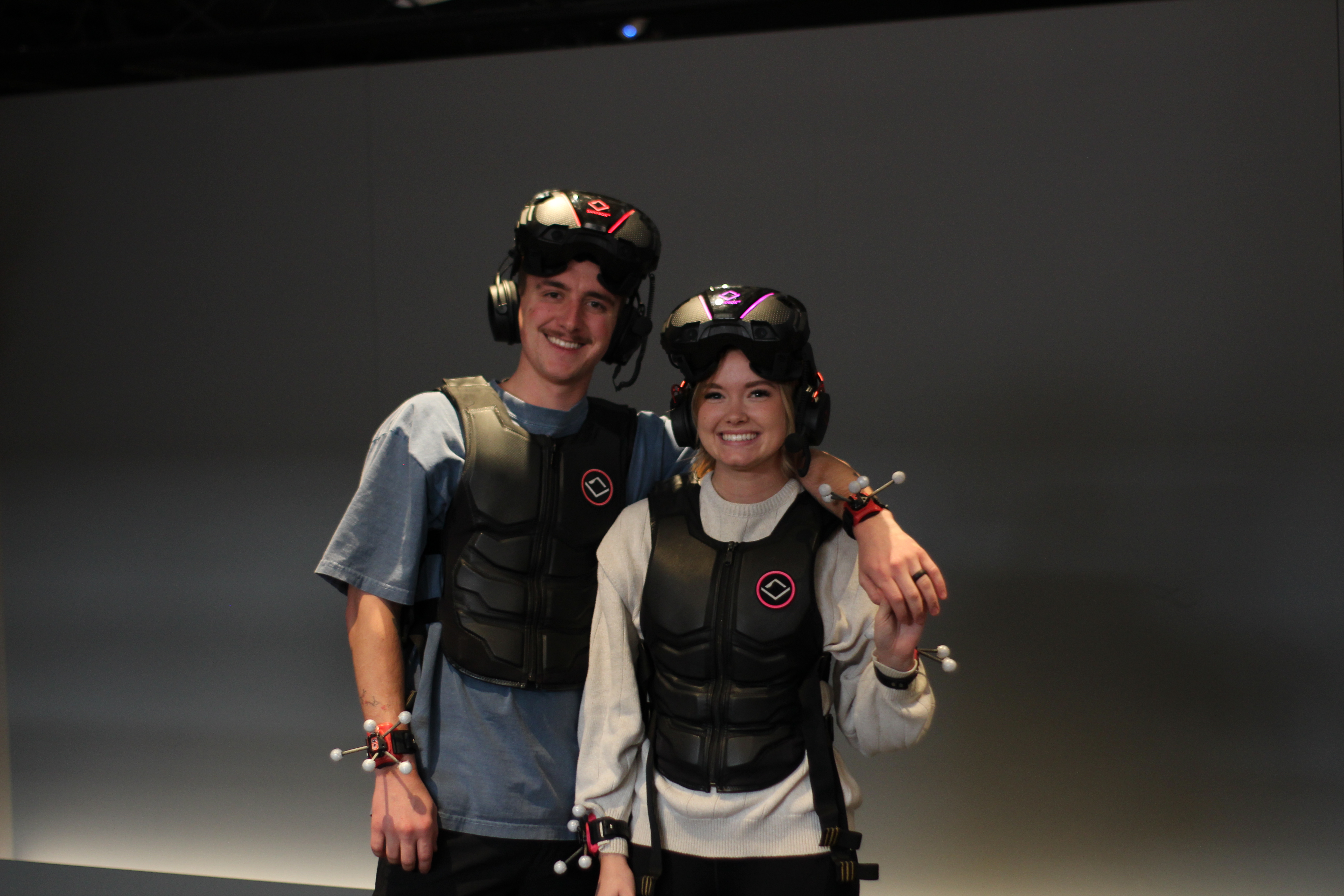 Couple with arm over shoulder geared up to play VR