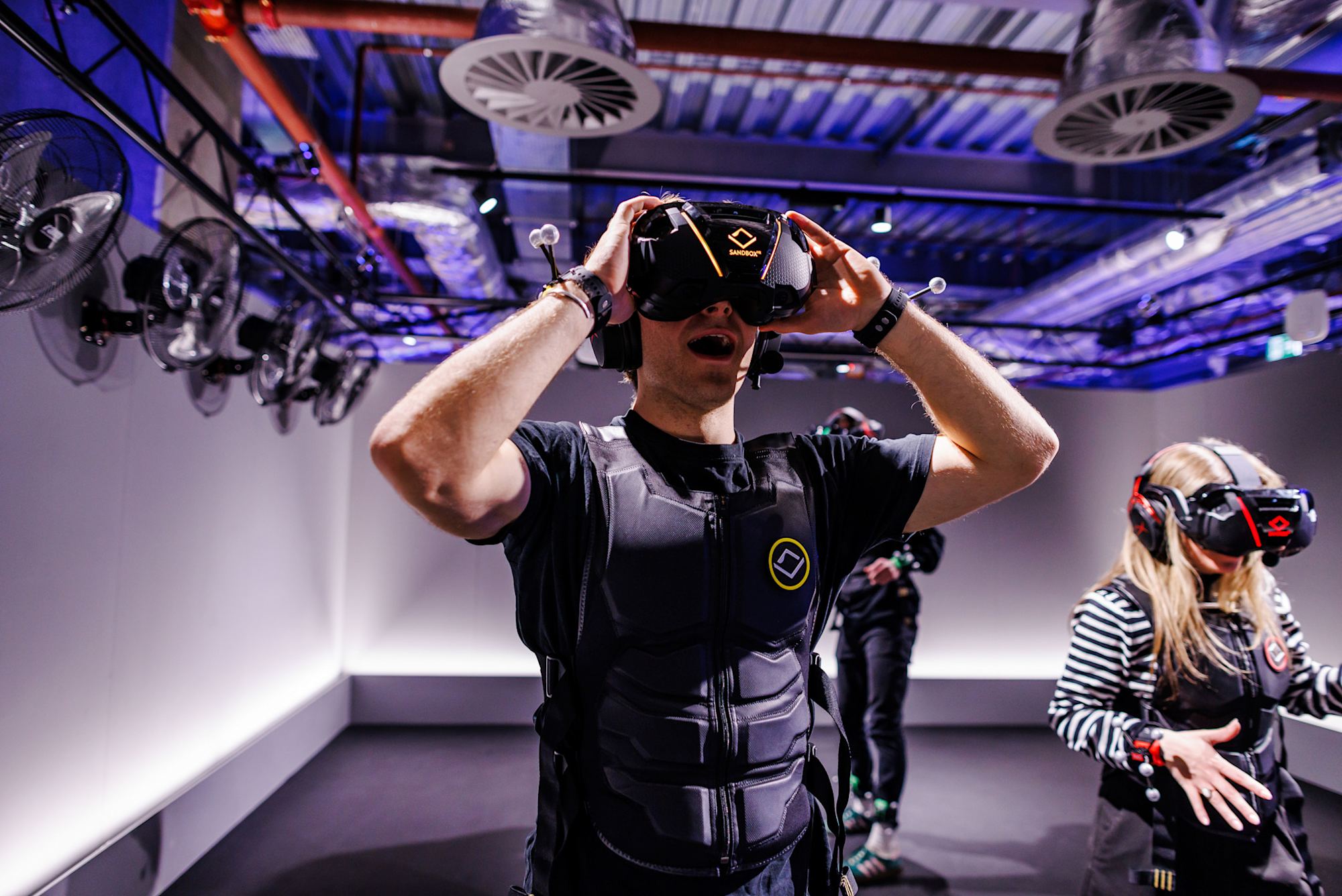 Spieler setzt ein VR-Headset auf, mit haptischer Weste und Trackern an den Handgelenken
