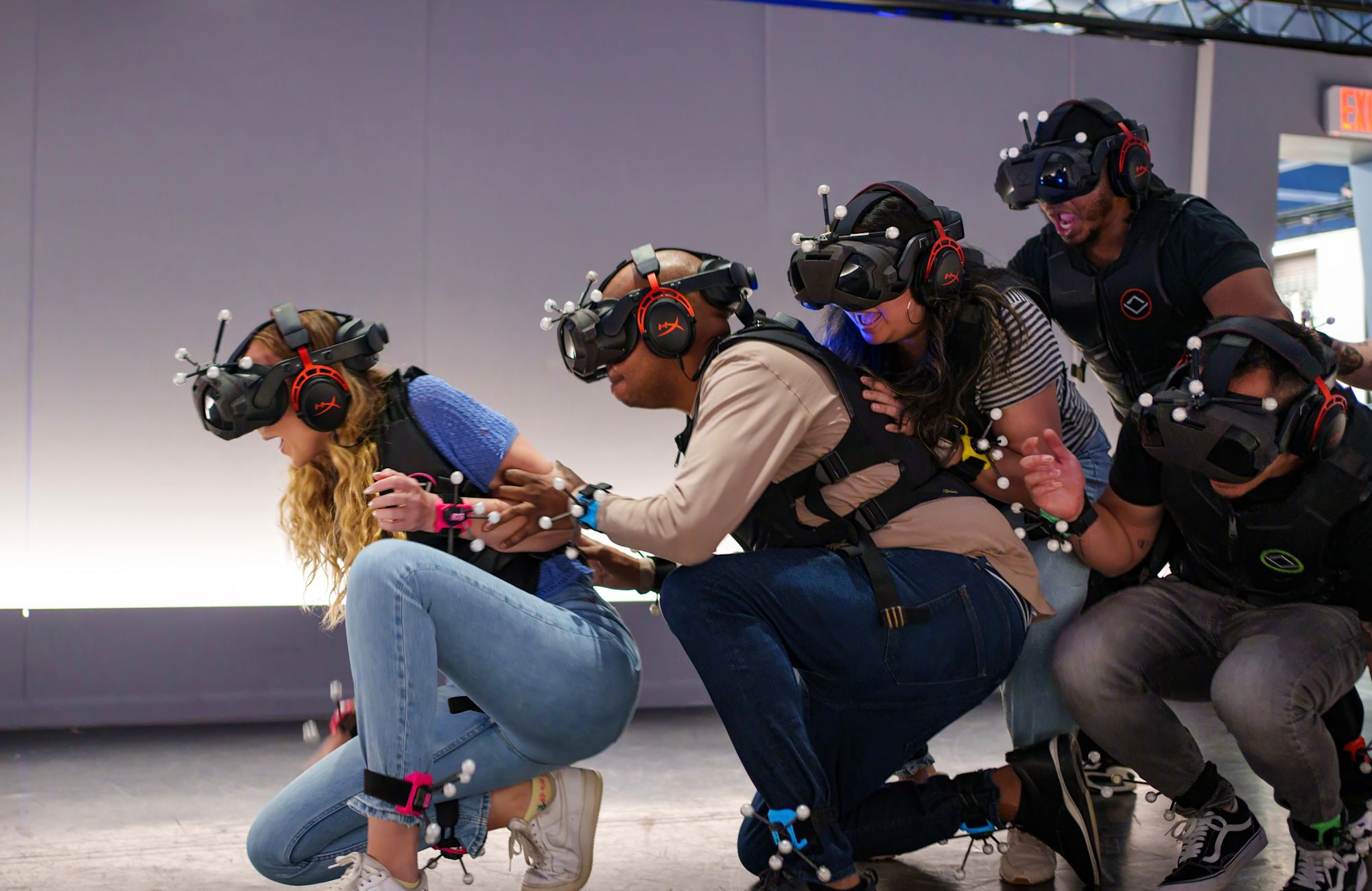 Gruppe mit VR-Headsets und Trackern an Händen und Füßen bewegt sich frei durch die Spielfläche