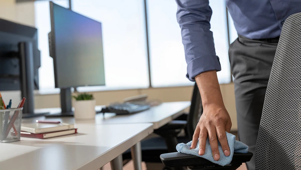 A hand cleaning the arm of a desk chair with a blue cloth