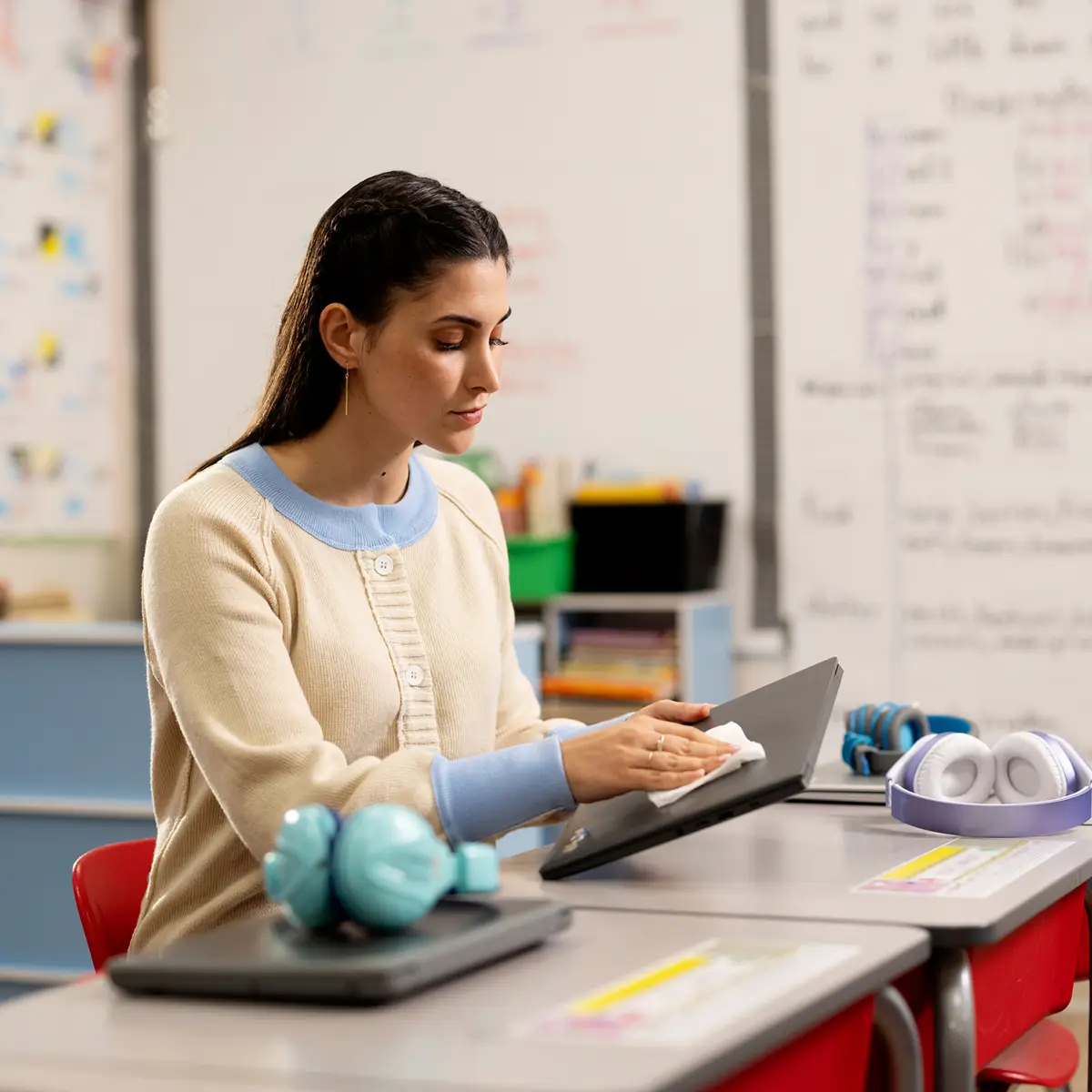Person wiping a tablet in a classroom with laptops and headphones nearby