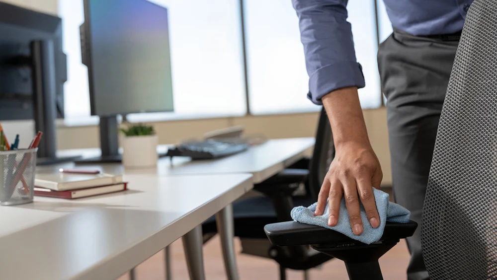 A hand wiping the arm rest of an office chair with a cloth