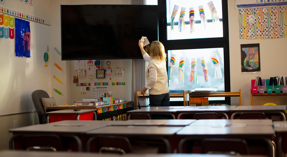 Teacher wiping a large monitor in a classroom with CloroxPro Screen+ Wipes