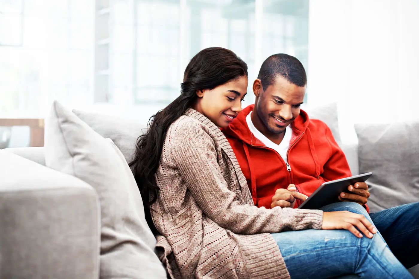 Couple sitting on a couch together, sharing a tablet in a cozy living room